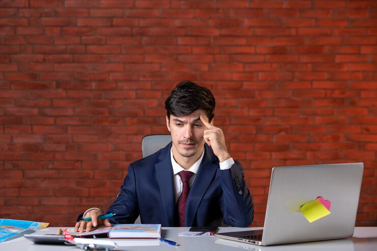 front-view-stressed-young-businessman-sitting-his-working-place-with-laptop-suit-work-plan-contractor-occupation-builder-business-job-corporate-project_461922-14461